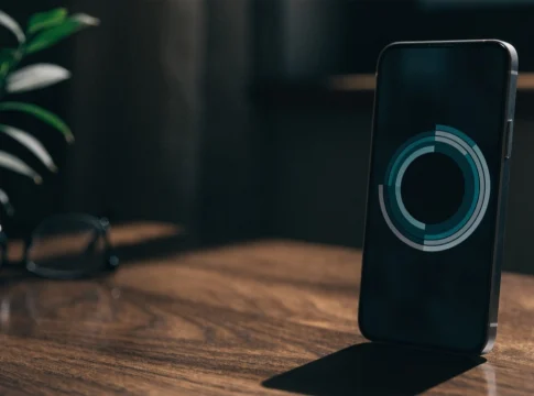 Telefon komórkowy leży pionowo na ciemnym drewnianym stole, a na ekranie wyświetla się okrągła grafika.