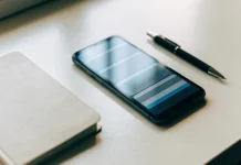 Celular deitado numa mesa clara ao lado de um caderno e uma caneta, exibindo uma lista
