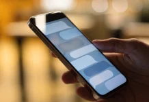 Celular na mão exibindo uma conversa com balões de mensagem, com fundo desfocado e quente