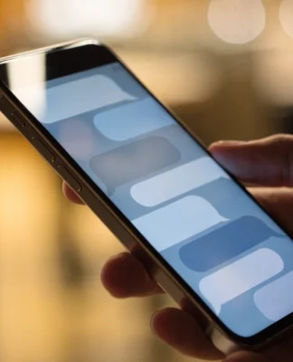 Un telefono cellulare tenuto in mano mostra una conversazione con fumetti di messaggio, su uno sfondo sfocato e caldo.