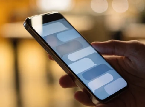 Celular na mão exibindo uma conversa com balões de mensagem, com fundo desfocado e quente