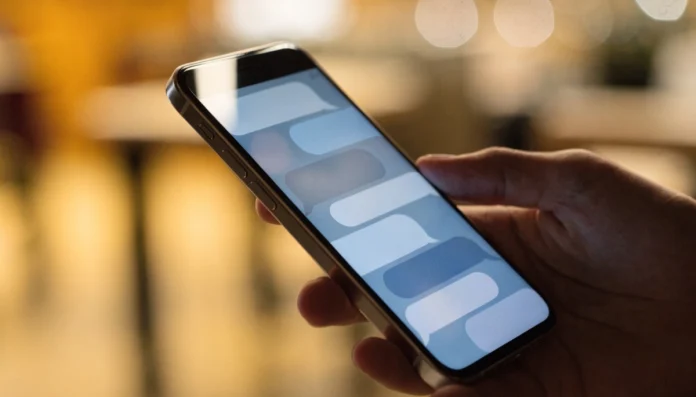 A cell phone in hand displays a conversation with message bubbles, against a blurred, warm background.