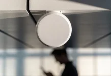 Ponto de acesso Wi-Fi branco e redondo fixado no teto, com uma pessoa desfocada usando o celular abaixo