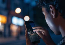 Pessoa fotografando uma rua escura à noite com o celular, e a tela mostra a cena bem mais clara