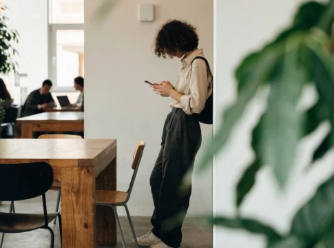 Osoba stoi przy ścianie z punktem dostępu Wi-Fi i patrzy na swój telefon komórkowy we wspólnej przestrzeni roboczej.