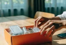 Mãos abrindo uma caixa laranja com pequenos produtos embalados sobre a mesa
