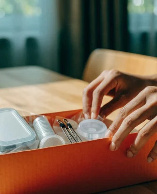 Mãos abrindo uma caixa laranja com pequenos produtos embalados sobre a mesa