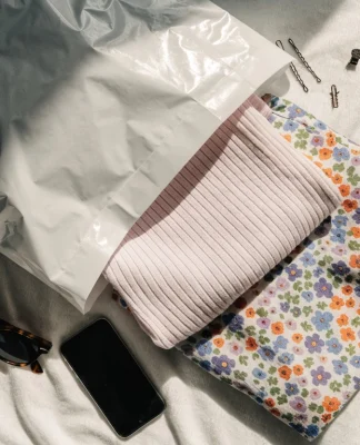 Op het bed lag een open wit pakket met opgevouwen kleren, een zonnebril en een mobiele telefoon.